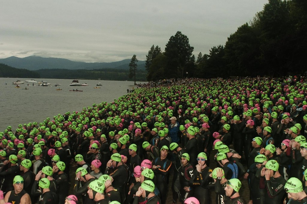Crowd of triathletes in wetsuits and bright green swim caps on a shoreline before an open-water swim start