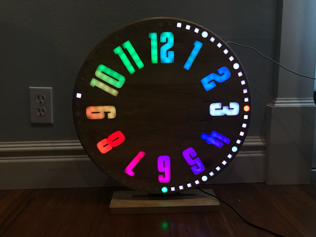 Large wooden LED clock with rainbow-lit numerals on a floor stand